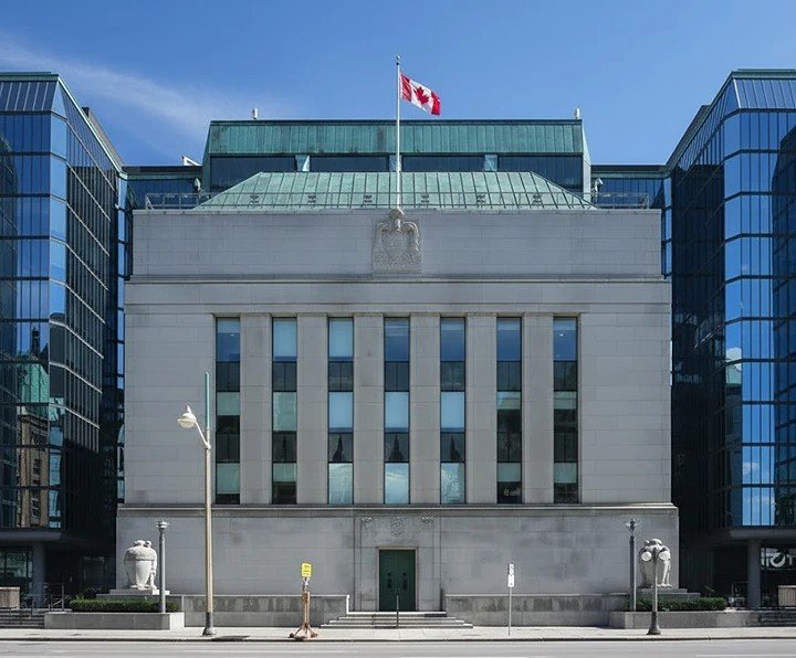 The modern glass and stone facade of the Bank of Canada headquarters building in Ottawa on a clear day.